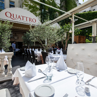 Outdoor dining area with tables set for service under a 'Quattro' restaurant canopy.